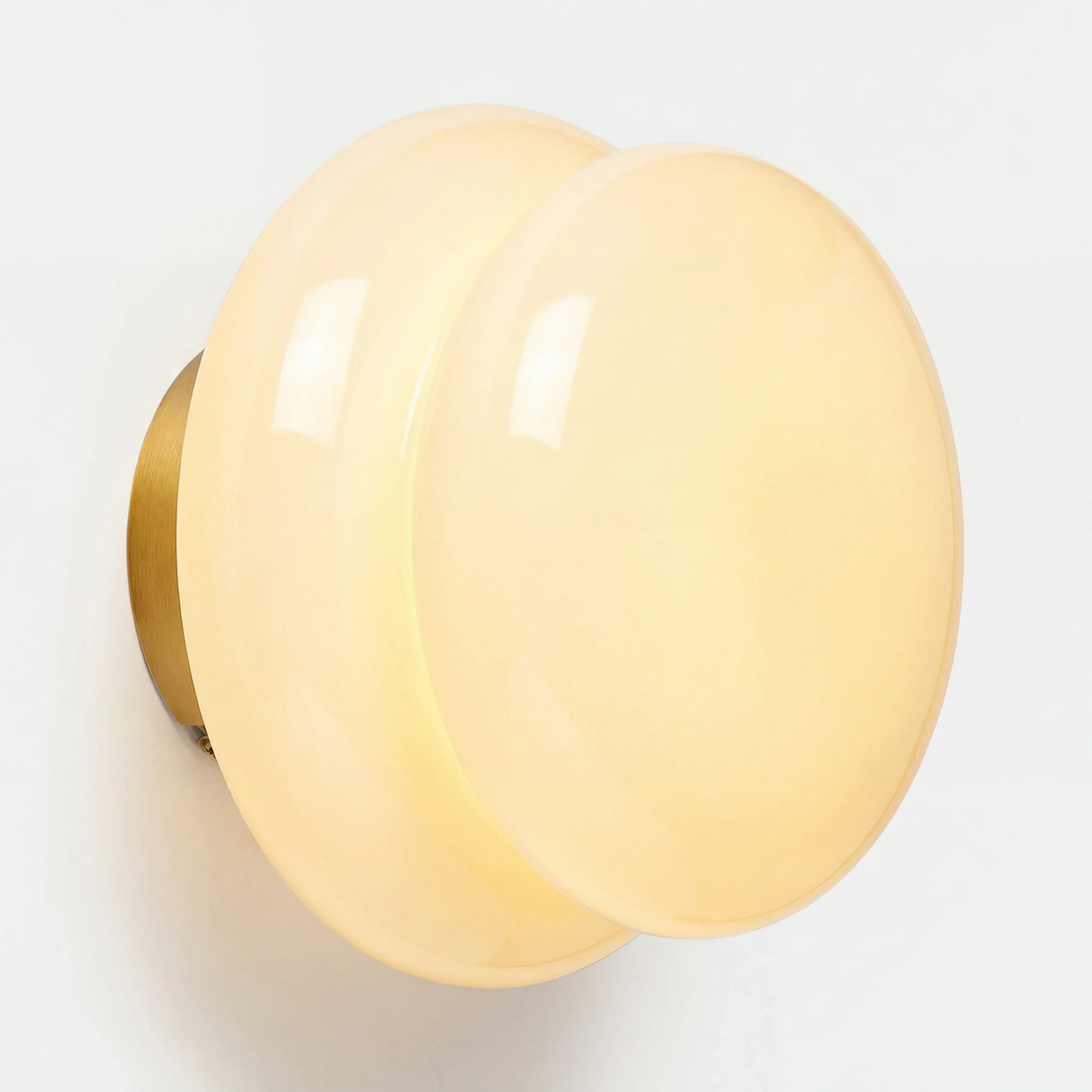 Cream opal glass wall sconce with brass backplate on white wall