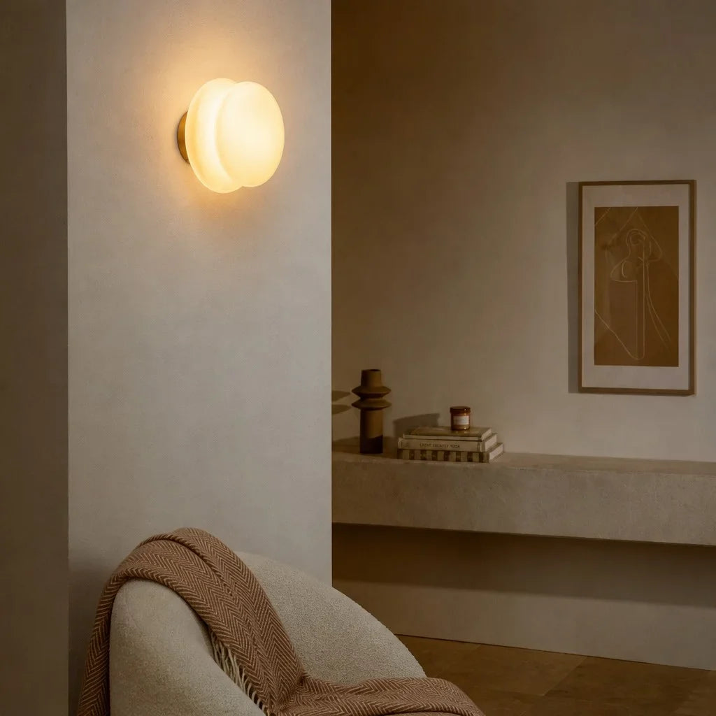 Lit opal wall sconce on plaster wall above a boucle chair