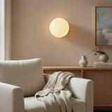 Lit opal glass wall sconce above a wood console beside white armchair