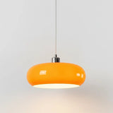 Orange oval glass pendant light hanging from a thin cord against a grey wall