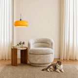 Orange glass pendant light over a boucle armchair with a cat resting nearby