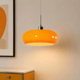 Orange oval glass pendant light beside framed wall art