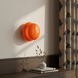 Orange opal glass wall sconce on white wall beside patterned curtain