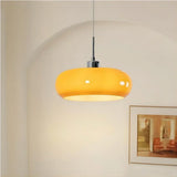 Orange lit glass pendant light against an arched wall with framed art