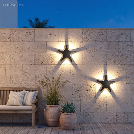 Starfish shaped wall light glowing on a rendered wall beside tropical planting