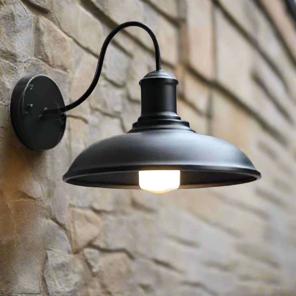Black gooseneck barn light lit on a pale stone wall