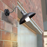 Gooseneck barn light lit on a red brick wall in daylight