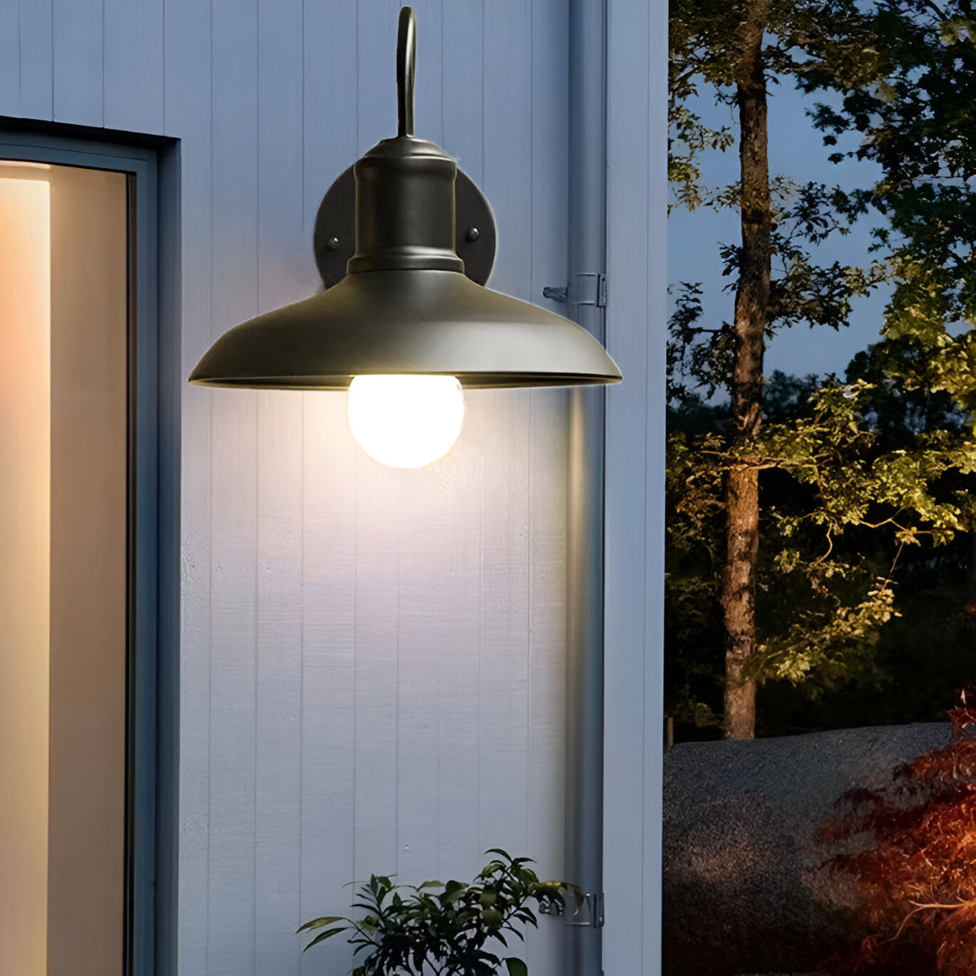 Gooseneck porch light lit on white cladding beside a doorway