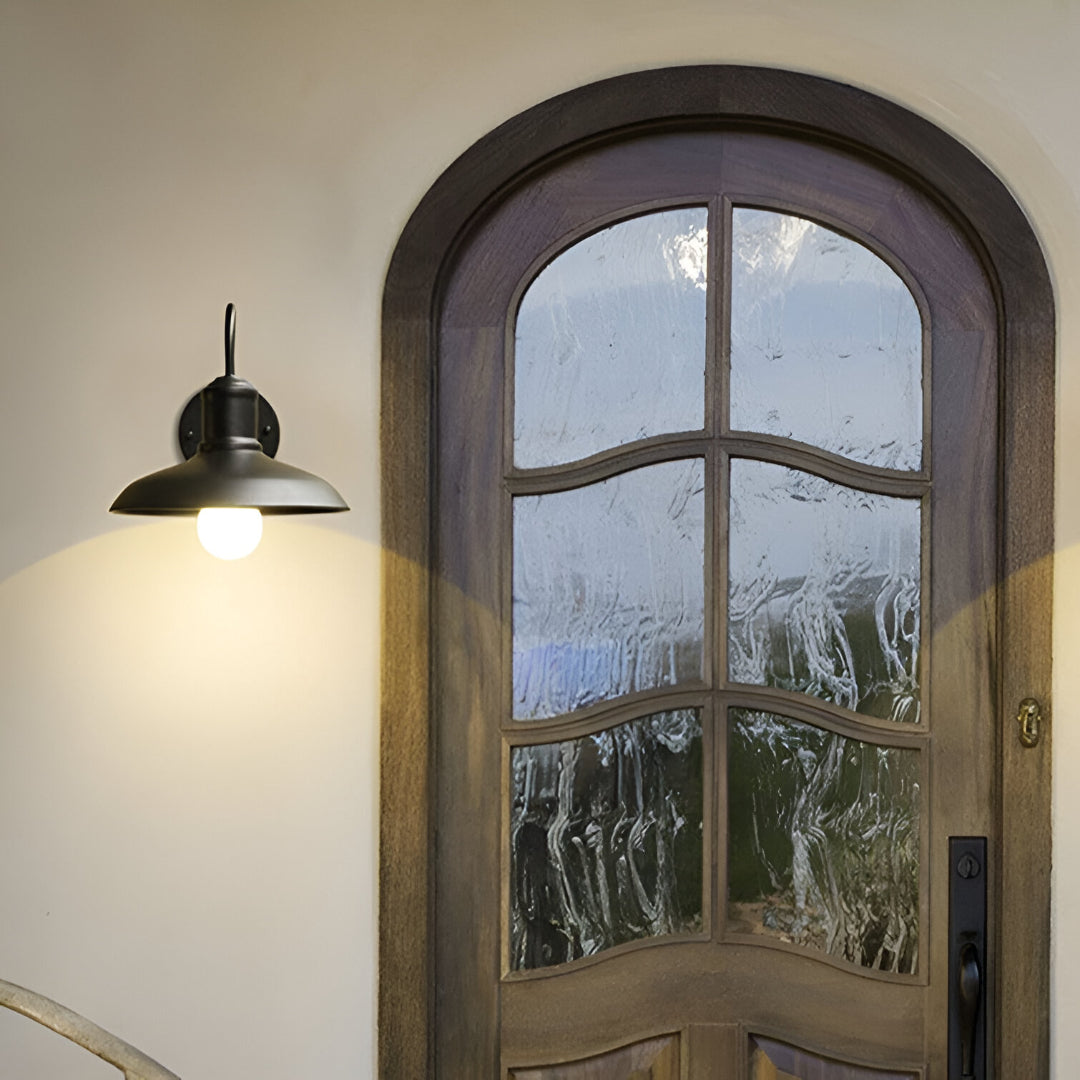 Gooseneck barn light lit above an arched timber front door