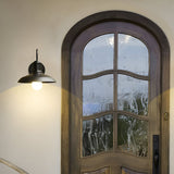 Gooseneck barn light lit above an arched timber front door