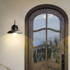 Gooseneck barn light lit above an arched timber front door