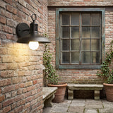 Gooseneck porch light lit on brick beside a green framed window