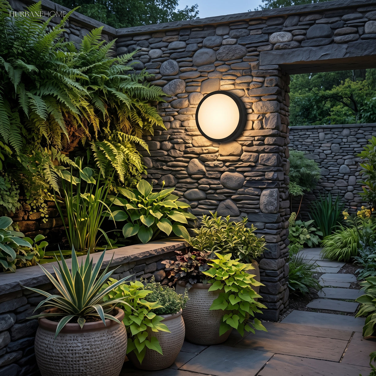 Round black porch light glowing on a stone wall beside patio seating
