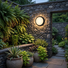 Round black porch light glowing on a stone wall beside patio seating