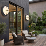 Round wall light lit on a terrace wall at dusk beside glazing