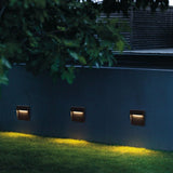 Three step lights lighting a dark wall above a green lawn