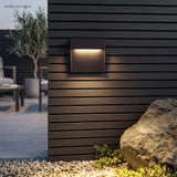 Square step light on dark timber cladding beside a rock and gravel bed