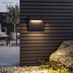 Square step light on dark timber cladding beside a rock and gravel bed