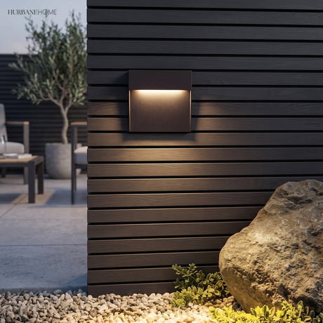 Square step light on dark timber cladding beside a rock and gravel bed