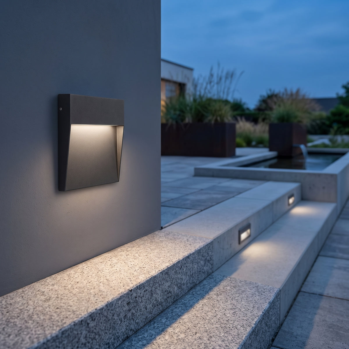 Square black step light washing a stone stair tread at dusk