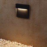 Step light on a rust coloured wall above white pebbles