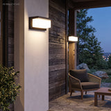 Two outdoor wall lights lit on dark timber cladding at dusk