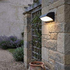 Outdoor light on a stone garden wall beside lavender and a trellis