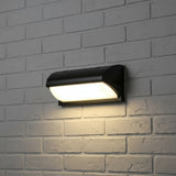 Curved wedge outdoor light lit on white painted brick at night