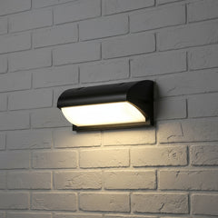 Curved wedge outdoor light lit on white painted brick at night