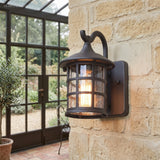 Lantern wall light on stone beside a glasshouse door and pots