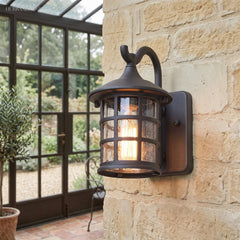 Lantern wall light on stone beside a glasshouse door and pots