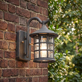 Lantern wall light on red brick beside a hedge of green leaves