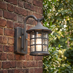 Lantern wall light on red brick beside a hedge of green leaves