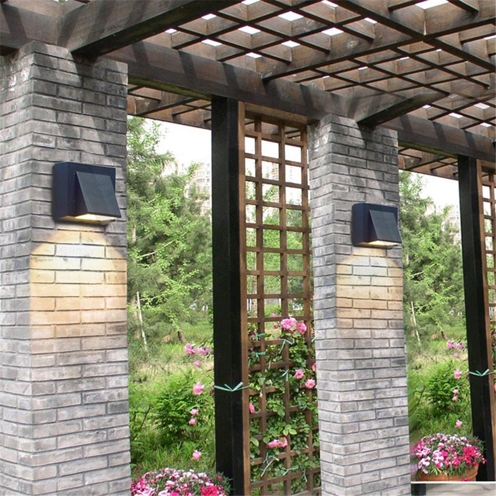 Two dark outdoor wall lights on brick pillars lighting a garden pergola