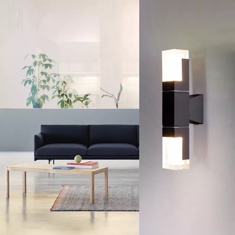 Prism tube wall sconce lit indoors on a white wall beside a sofa