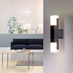 Prism tube wall sconce lit indoors on a white wall beside a sofa