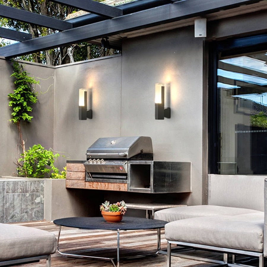 Two prism tube wall sconces lit on a concrete wall above a patio