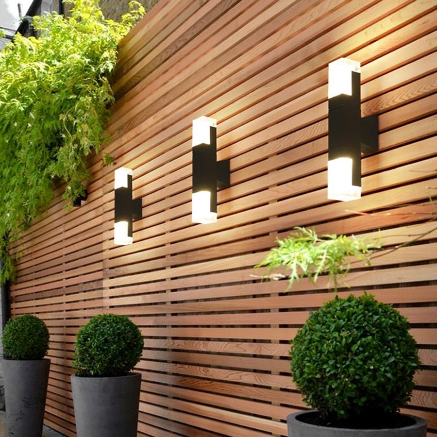 Three prism tube wall sconces lit on a slatted timber garden wall
