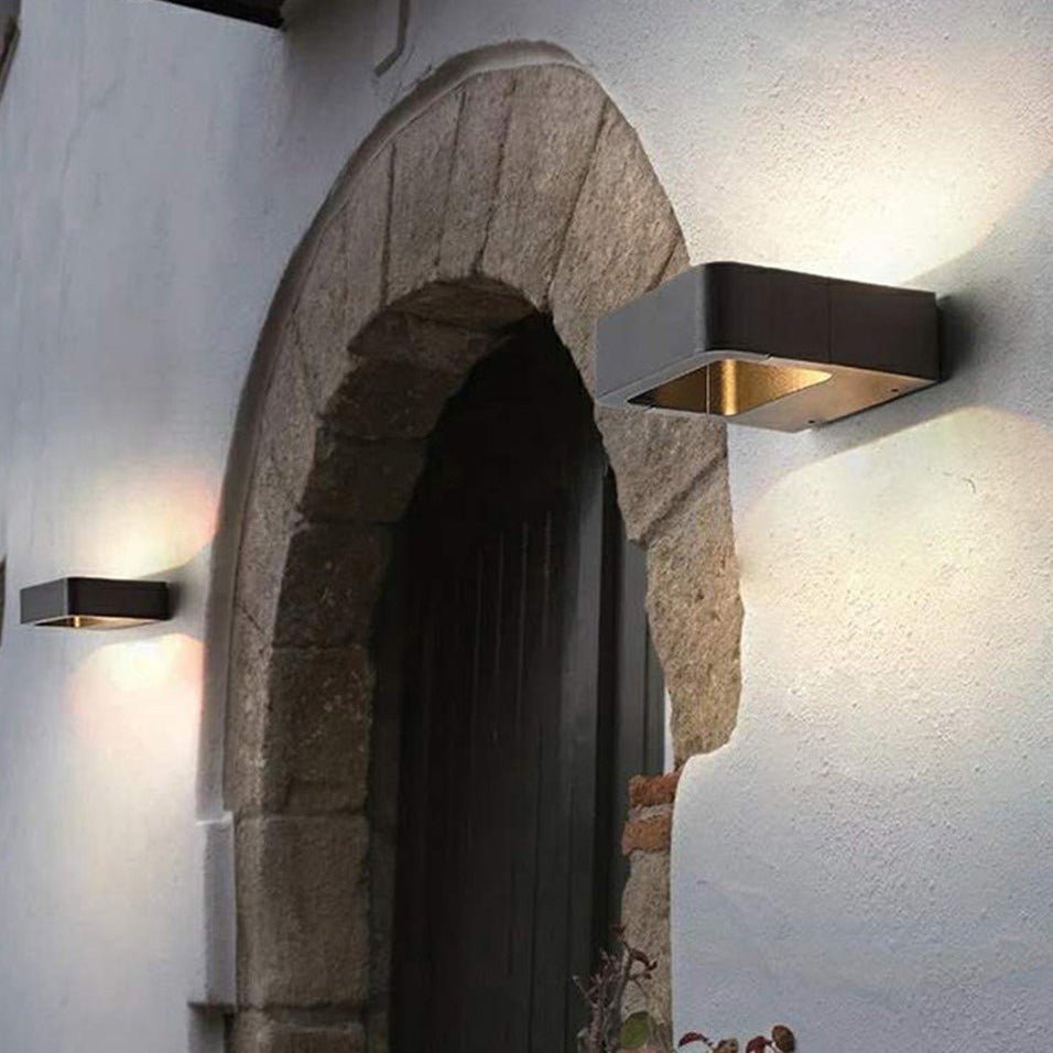Outdoor wall sconce lit beside a stone archway and a white wall