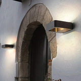 Outdoor wall sconce lit beside a stone archway and a white wall