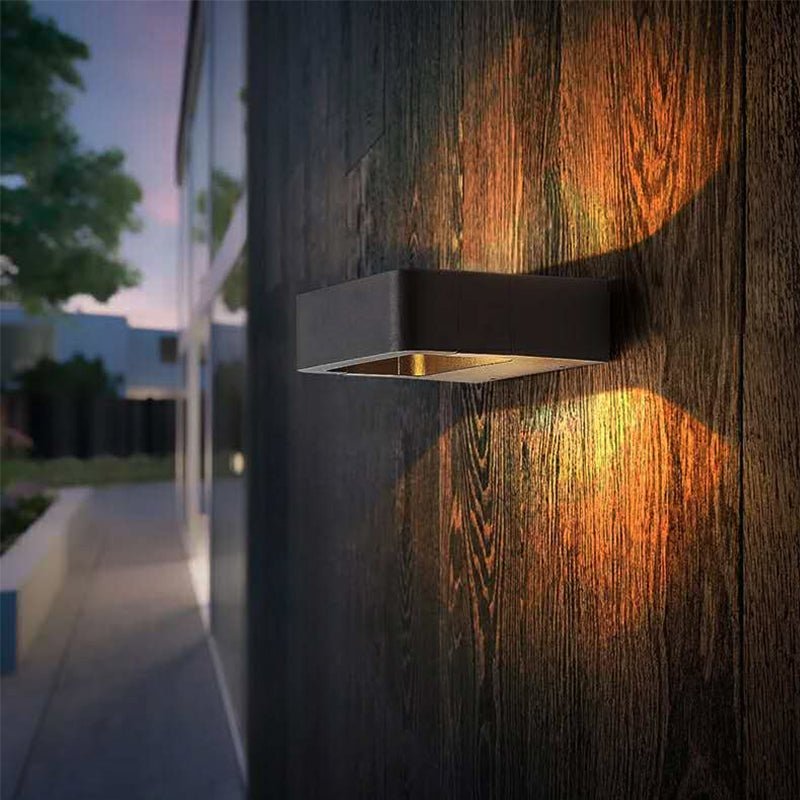 Outdoor wall sconce lit on a dark timber wall along a garden path