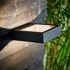 Dark outdoor wall sconce lit on a stone wall beside green bamboo