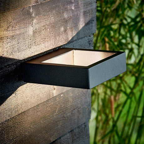 Dark outdoor wall sconce lit on a stone wall beside green bamboo