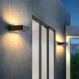 Two outdoor wall sconces lit up and down a grey rendered house wall