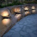Three outdoor wall sconces lit along a curved dry stone garden wall