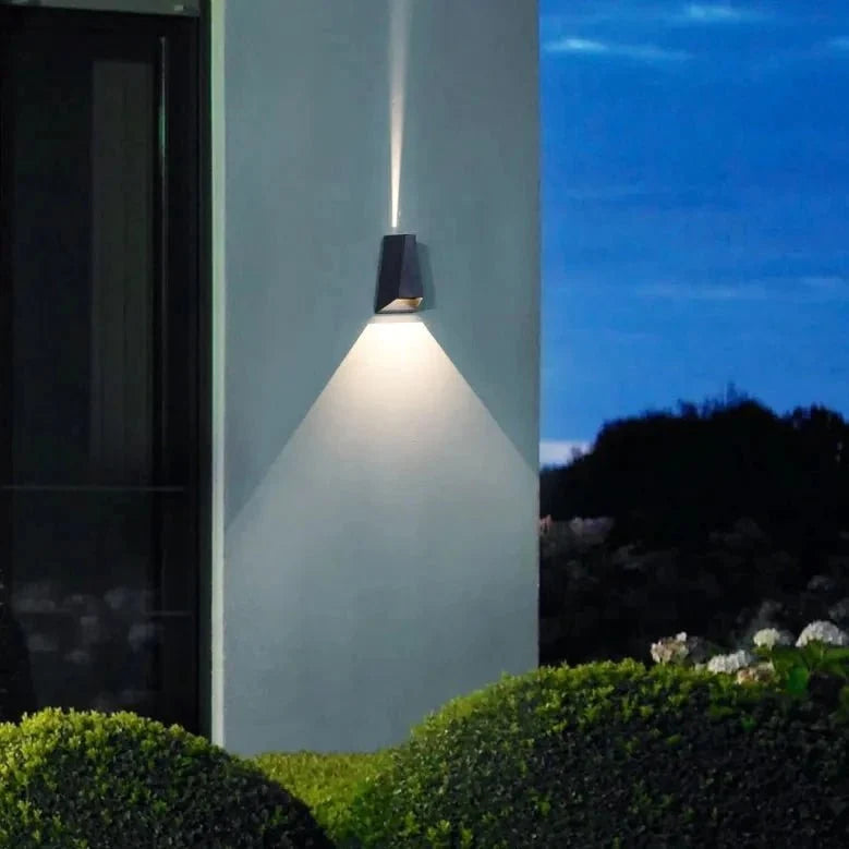 Single outdoor sconce lighting a garden wall above clipped hedging
