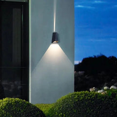Single outdoor sconce lighting a garden wall above clipped hedging
