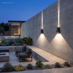 Two outdoor sconces lighting a concrete garden wall beside a lit pool
