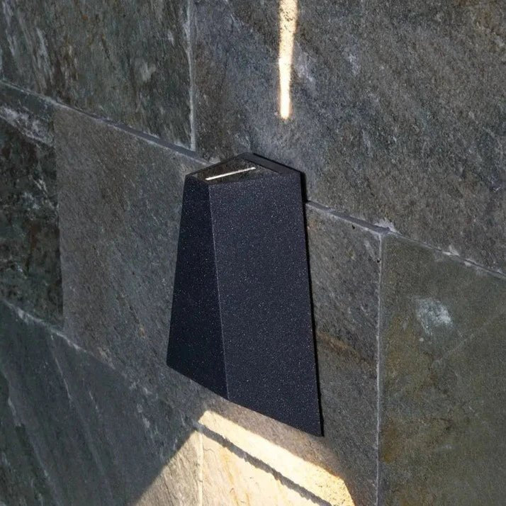 Wedge sconce mounted on a grey stone wall with light below