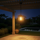 A black metal outdoor pendant light hangs over a wooden dining table and wicker chairs on a covered patio, with a pool and greenery in the background at sunset.